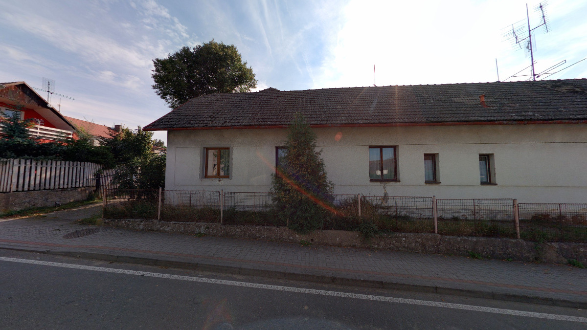 Pohled z ulice na podlouhlý přízemní rodinný dům Želeč 41 se světlou fasádou, tmavou šikmou střechou a plotem podél silnice